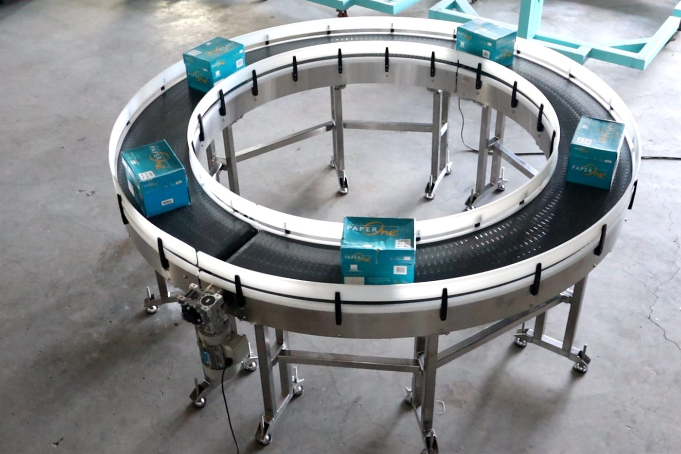 A complete NEXUS curve conveyor carrying cartons around a full loop on the factory floor, both ends of the machine in view.