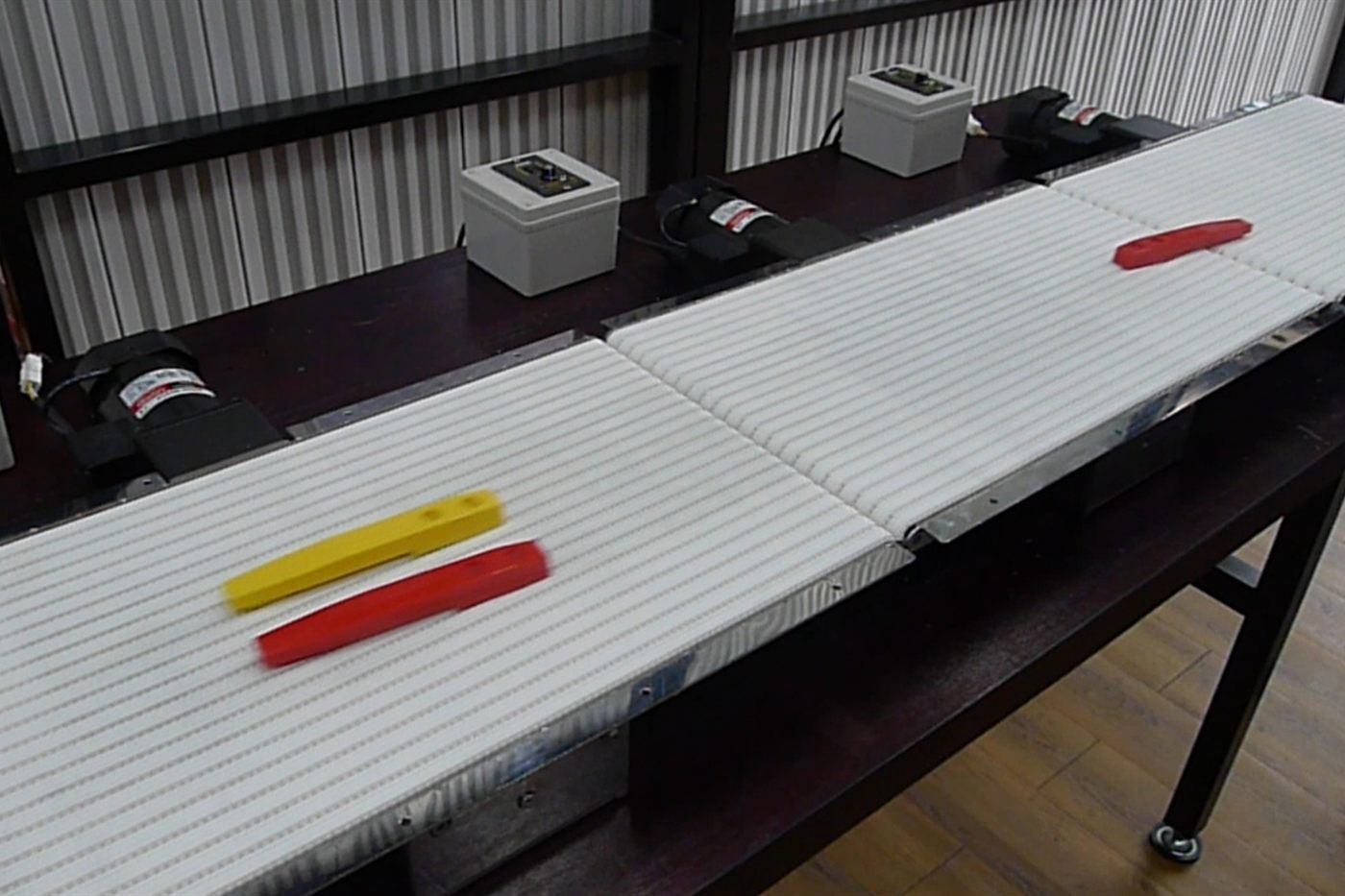 Two NEXUS miniature conveyors set end to end, moving small items between two machines.