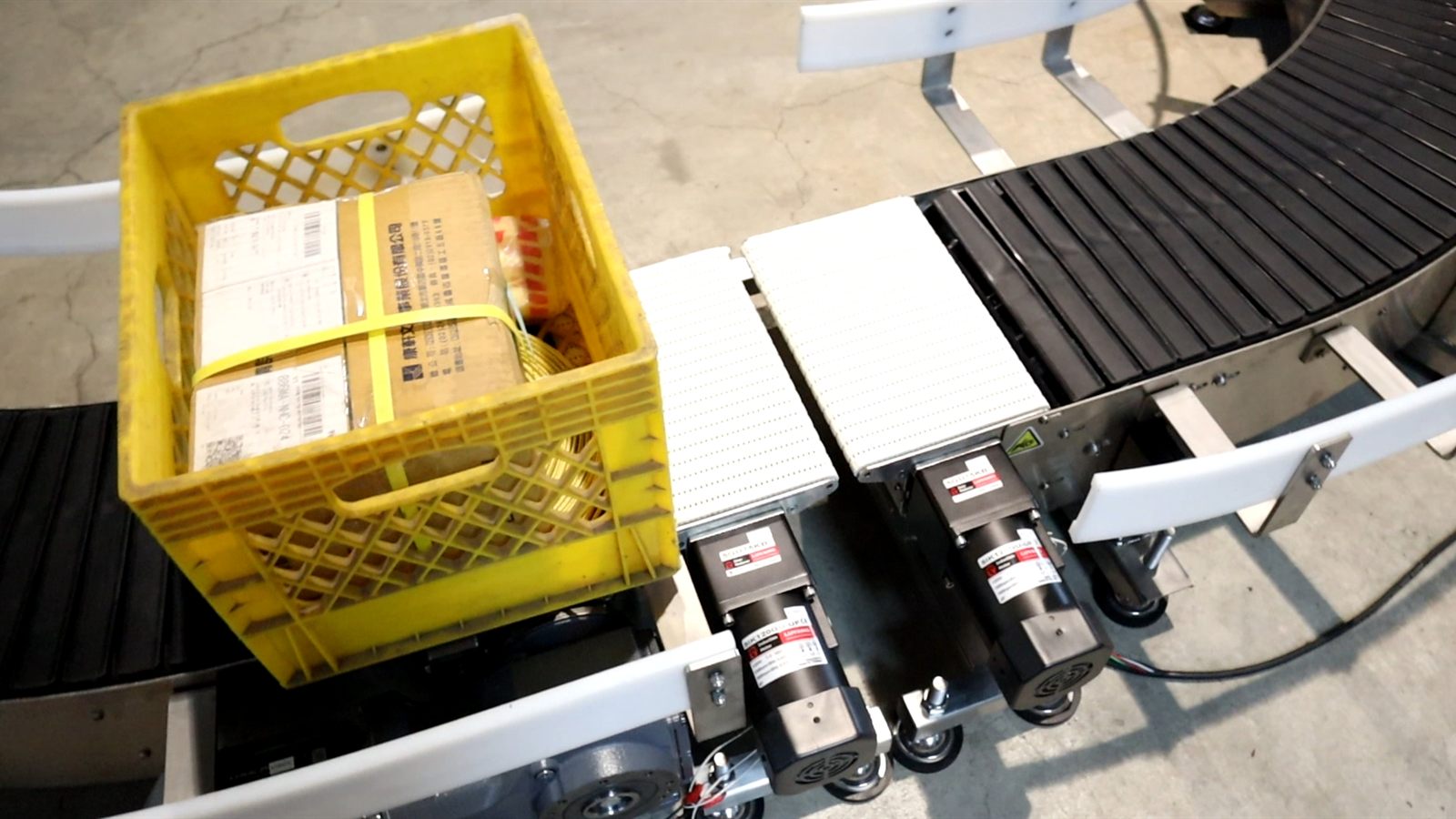 A plastic crate transferring from a spiral conveyor onto a connected curve conveyor.