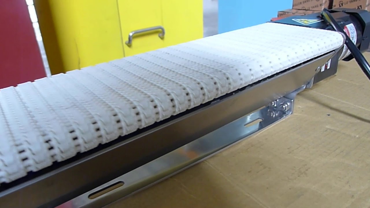 A wide miniature conveyor with a white modular belt on a stainless steel frame.