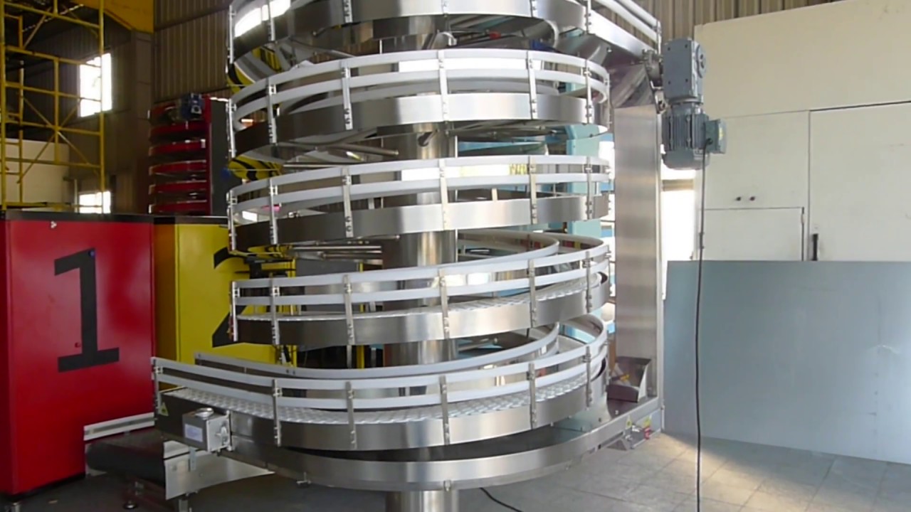 A stainless steel narrow track spiral conveyor with several tiers standing in a factory.