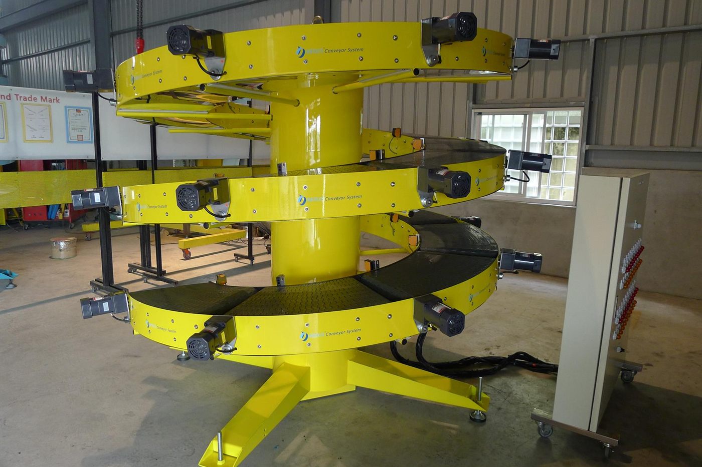 A yellow NEXUS Zone-Controlled Spiral Buffer in the factory, with a gearmotor on each curved conveying unit.