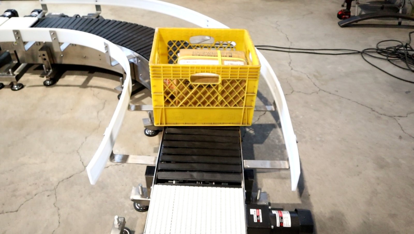 A single yellow plastic crate resting on the straight section of the integrated curve conveyor during a factory test.