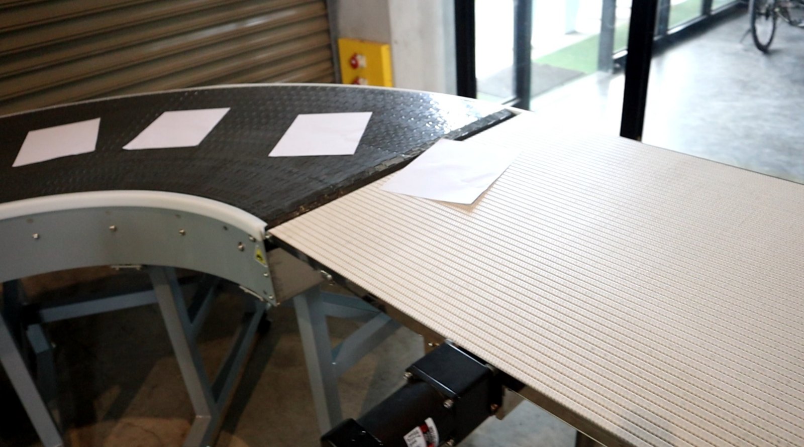 Close view of the modular plastic belt on a curve conveyor, with sheets of paper resting on the surface, in the NEXUS factory.